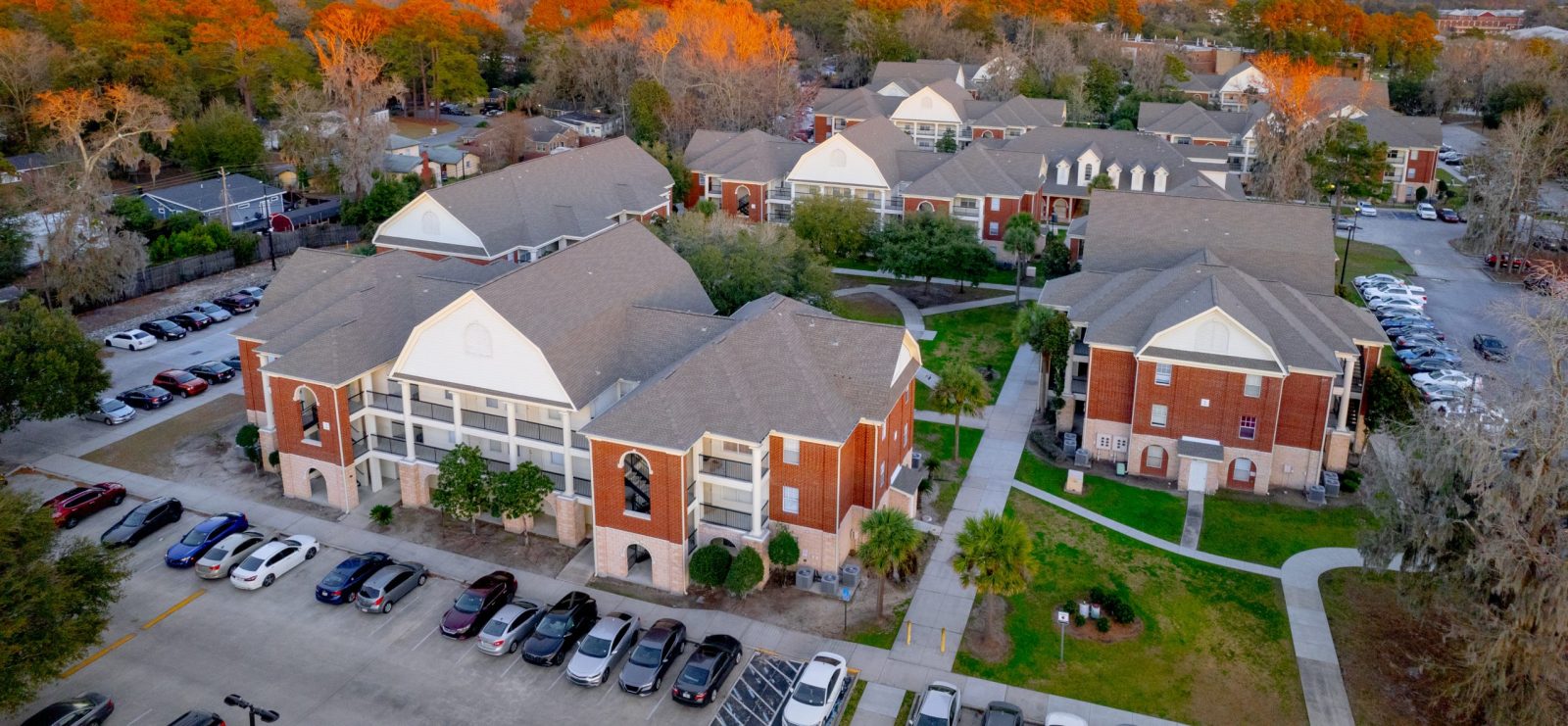 Brick multi-story buildings with full parking lot of cars during fall.